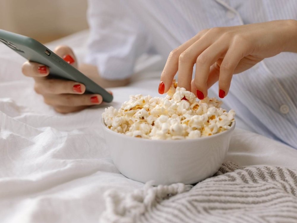 Person with Red Nails Using a Smartphone while Eating Popcorn
